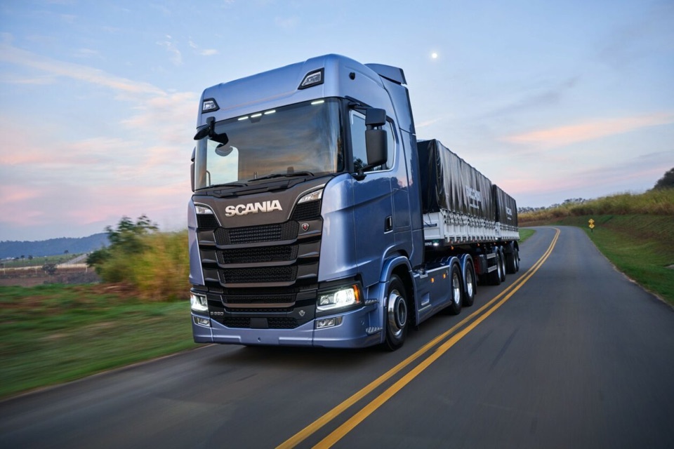 Caminhão rodoviário Scania azul em estrada ao entardecer